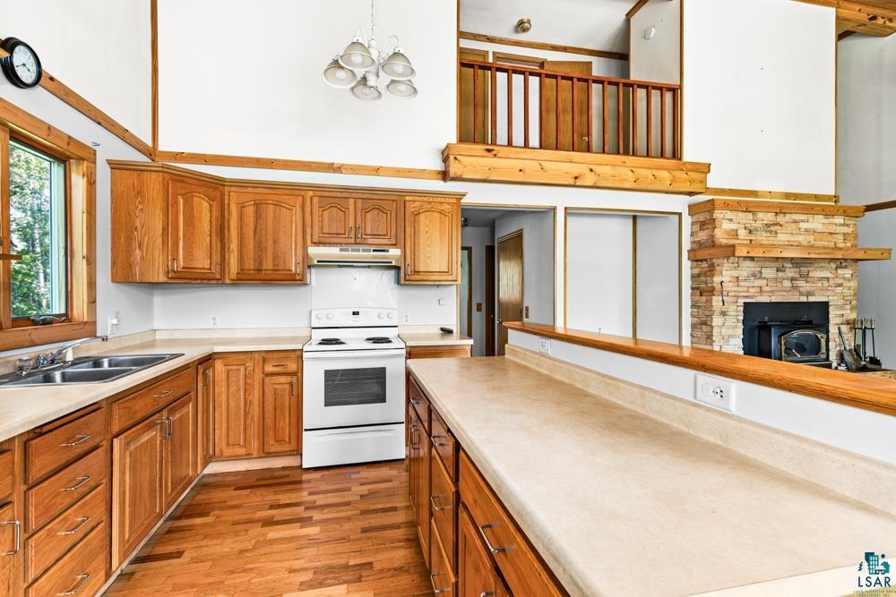 740 Seboe Road Wrenshall, MN 55797 - Photo 10 of 20 Kitchen with a notable chandelier, a fireplace, white electric range, light wood-type flooring, and sink
