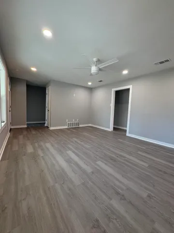 a view of an empty room with wooden floor and a ceiling fan