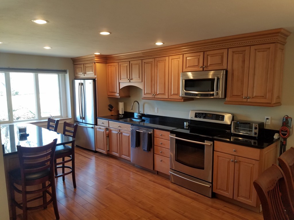174 Lowell Road, Unit 82 Mashpee, MA 02649 - Photo 2 of 16 a kitchen with kitchen island granite countertop wooden floors wooden cabinets dining table and stainless steel appliances