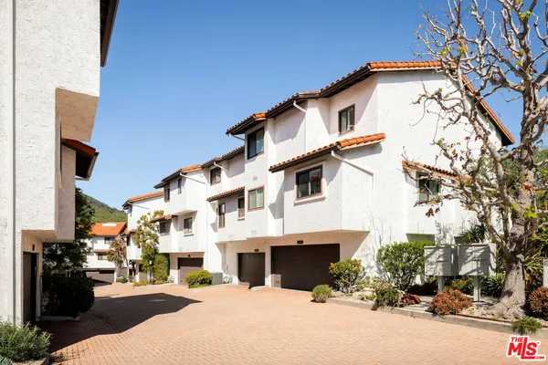 a view of a white building among the street with potted plants