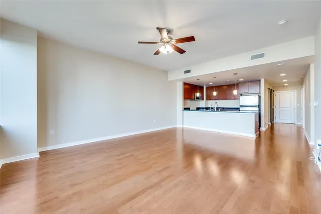 a view of an empty room and kitchen view with wooden floor
