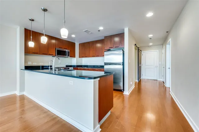 a kitchen with stainless steel appliances granite countertop a refrigerator a oven a sink and a dining table with wooden floor