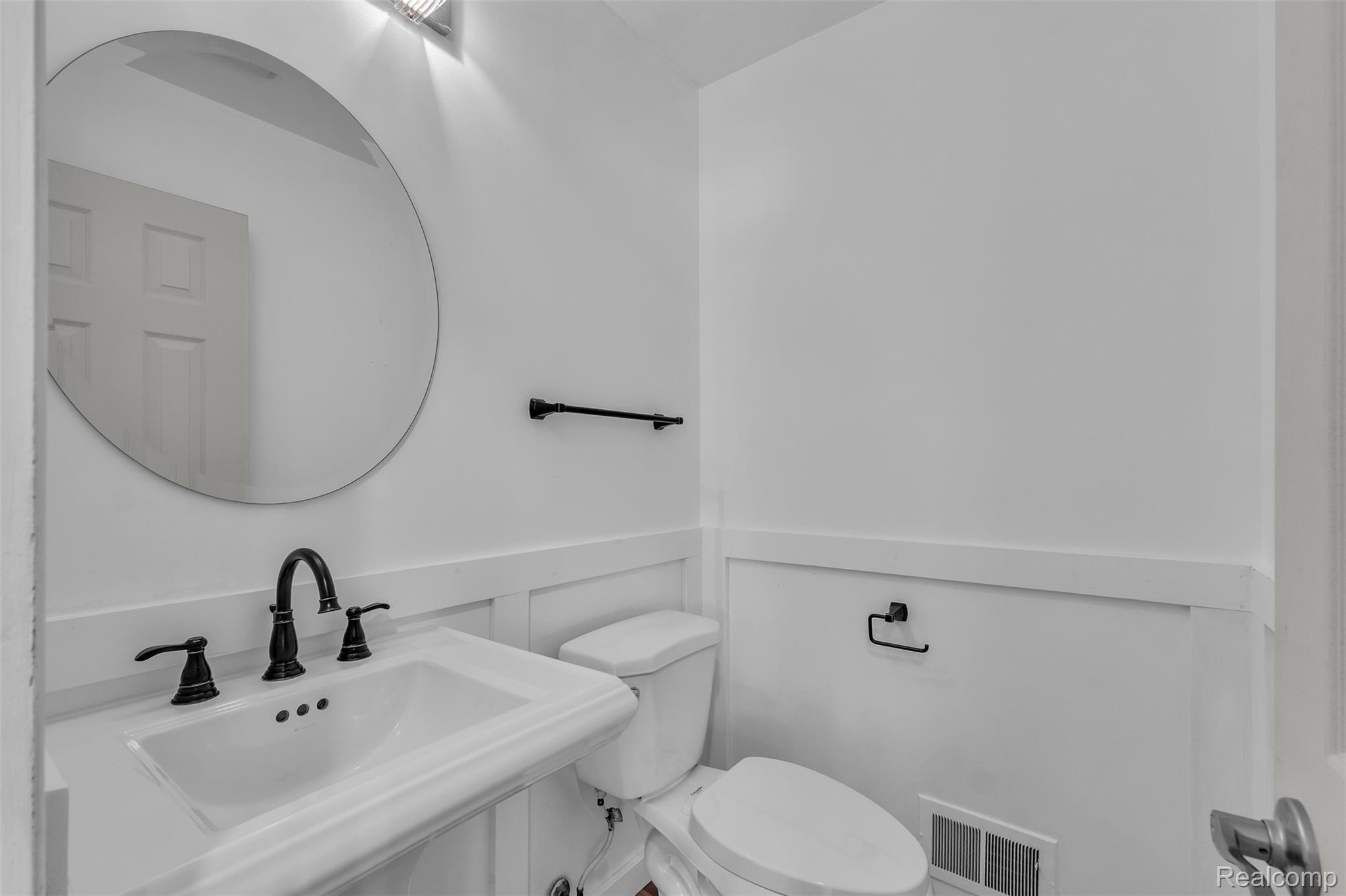 7000 Woonsocket Street Canton, MI 48187 - Photo 34 of 65 Pedestal sink with matte black faucet, round wall mirror, and wainscoting detailing