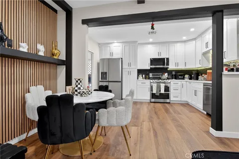 a kitchen with stainless steel appliances kitchen island granite countertop a stove a sink a refrigerator white cabinets wooden floor and a dining table