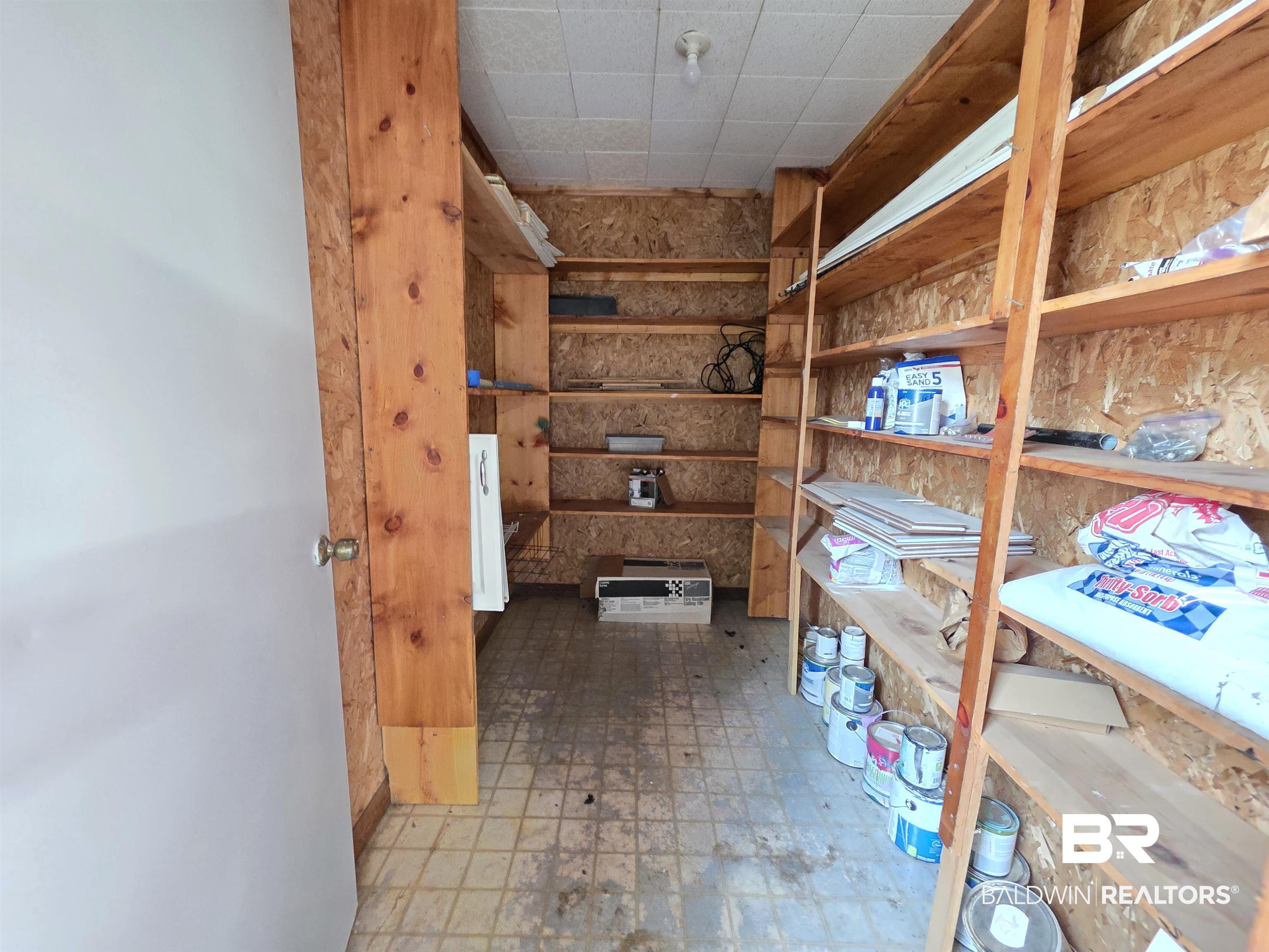 558 Stanton Road Atmore, AL 36502 - Photo 25 of 29 Storage room featuring extensive built-in wooden shelving, durable tile flooring, and a drop ceiling
