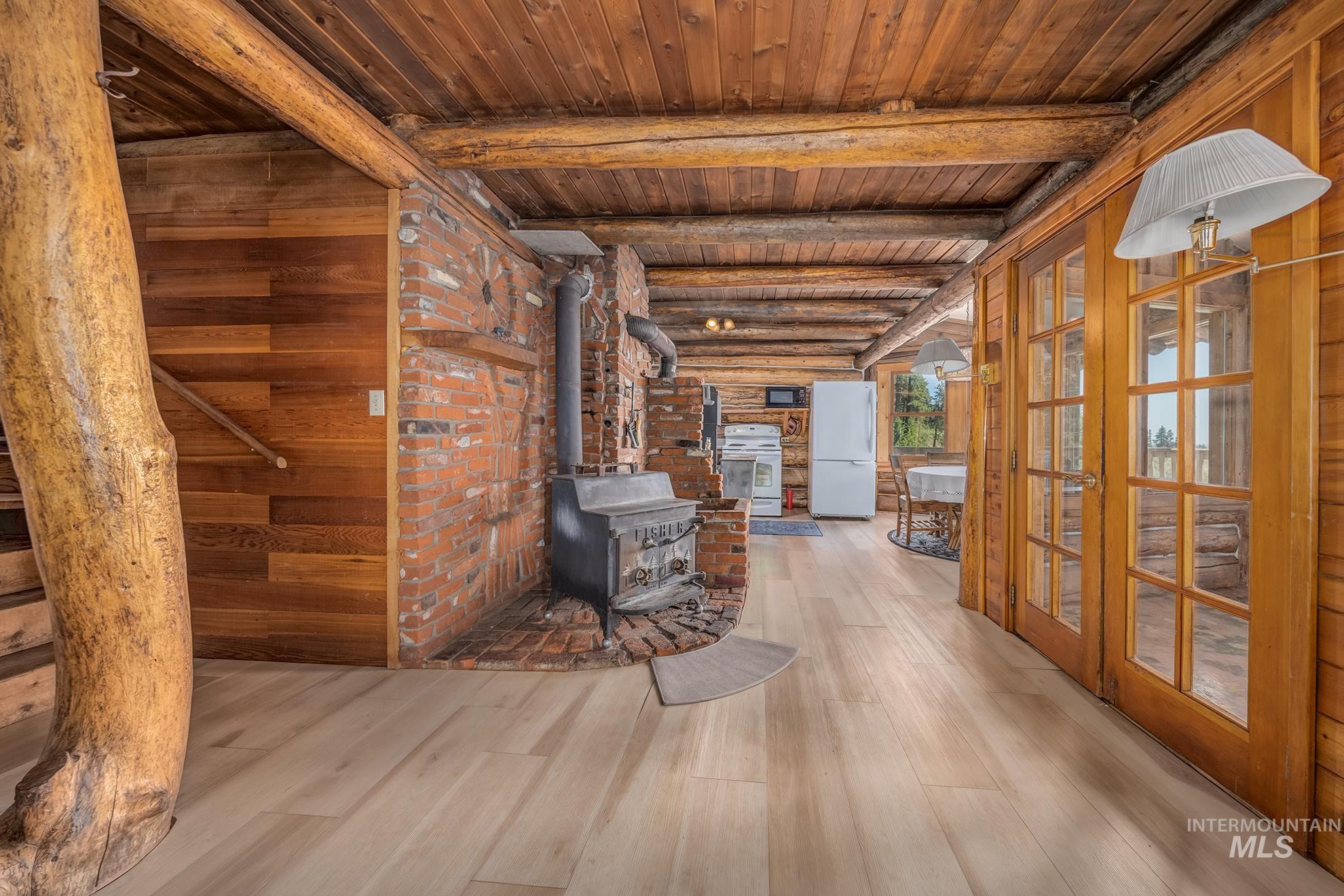 2150 Seid Creek Road Cambridge, ID 83610 - Photo 10 of 50 Interior space featuring light wood-finish flooring, exposed log beam ceiling, and a prominent brick-clad wood-burning stove with a stone hearth