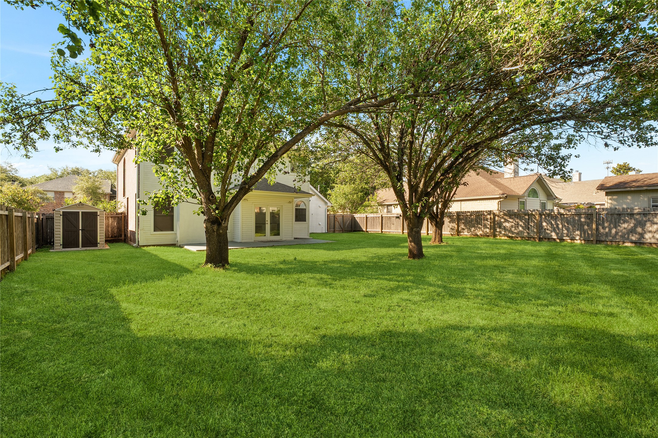 206 River Down Road Georgetown, TX 78628 - Photo 38 of 39 Spacious backyard featuring a large green lawn, mature trees, a privacy fence, and a patio with double-door access to the home