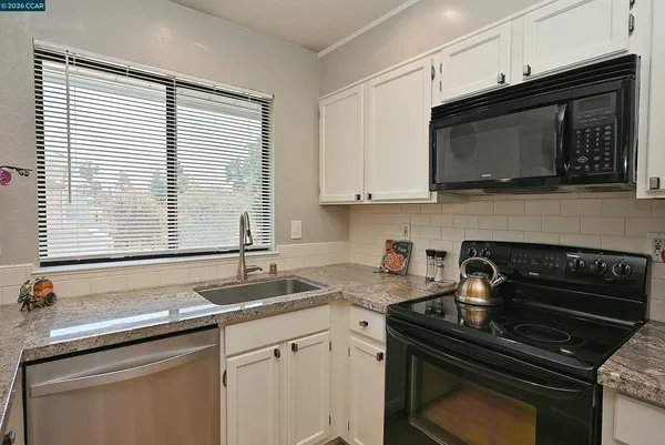 a kitchen with granite countertop white cabinets appliances and a sink