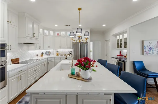 a kitchen with kitchen island granite countertop a dining table chairs sink and white cabinets