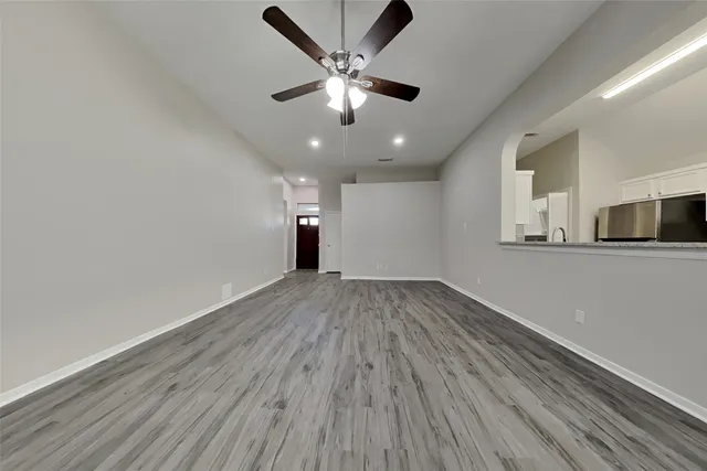 a view of an empty room with wooden floor and a ceiling fan