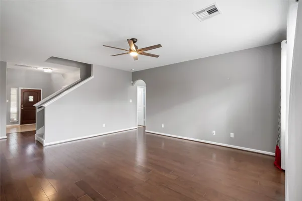 a view of an empty room with wooden floor and a ceiling fan