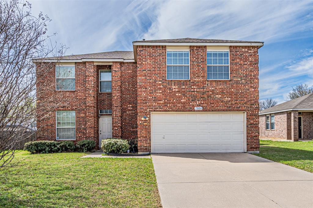 Traditional home featuring a front lawn, concrete driveway, brick siding, and an attached garage