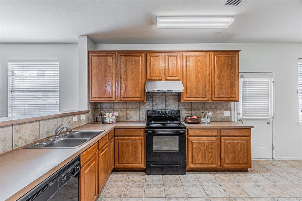 7804 Hidden Path Lane Denton, TX 76210 - Photo 11 of 40 Kitchen with black appliances, wood finish cabinets, light countertops, decorative backsplash, and a textured ceiling