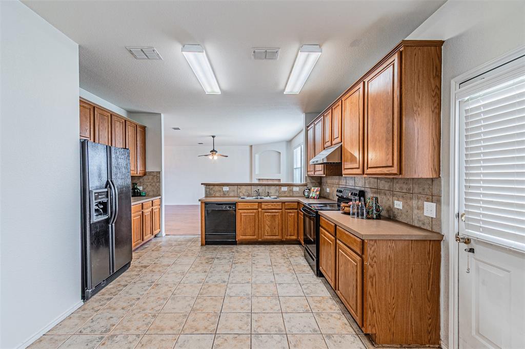7804 Hidden Path Lane Denton, TX 76210 - Photo 13 of 40 Kitchen with black appliances, light countertops, wood finish cabinets, and decorative backsplash