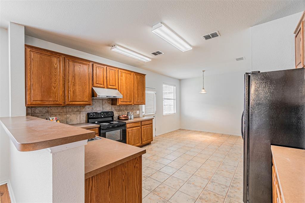 7804 Hidden Path Lane Denton, TX 76210 - Photo 10 of 40 Kitchen featuring black appliances, wood finish cabinetry, a peninsula, decorative light fixtures, and light countertops