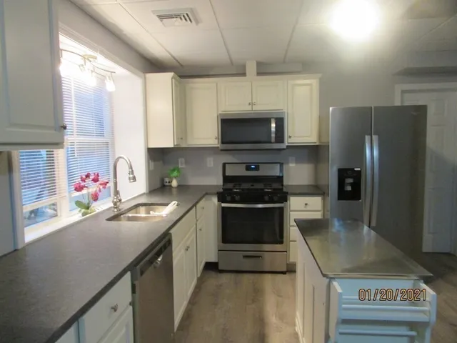 a kitchen with stainless steel appliances a sink a stove a microwave a refrigerator a sink and cabinets