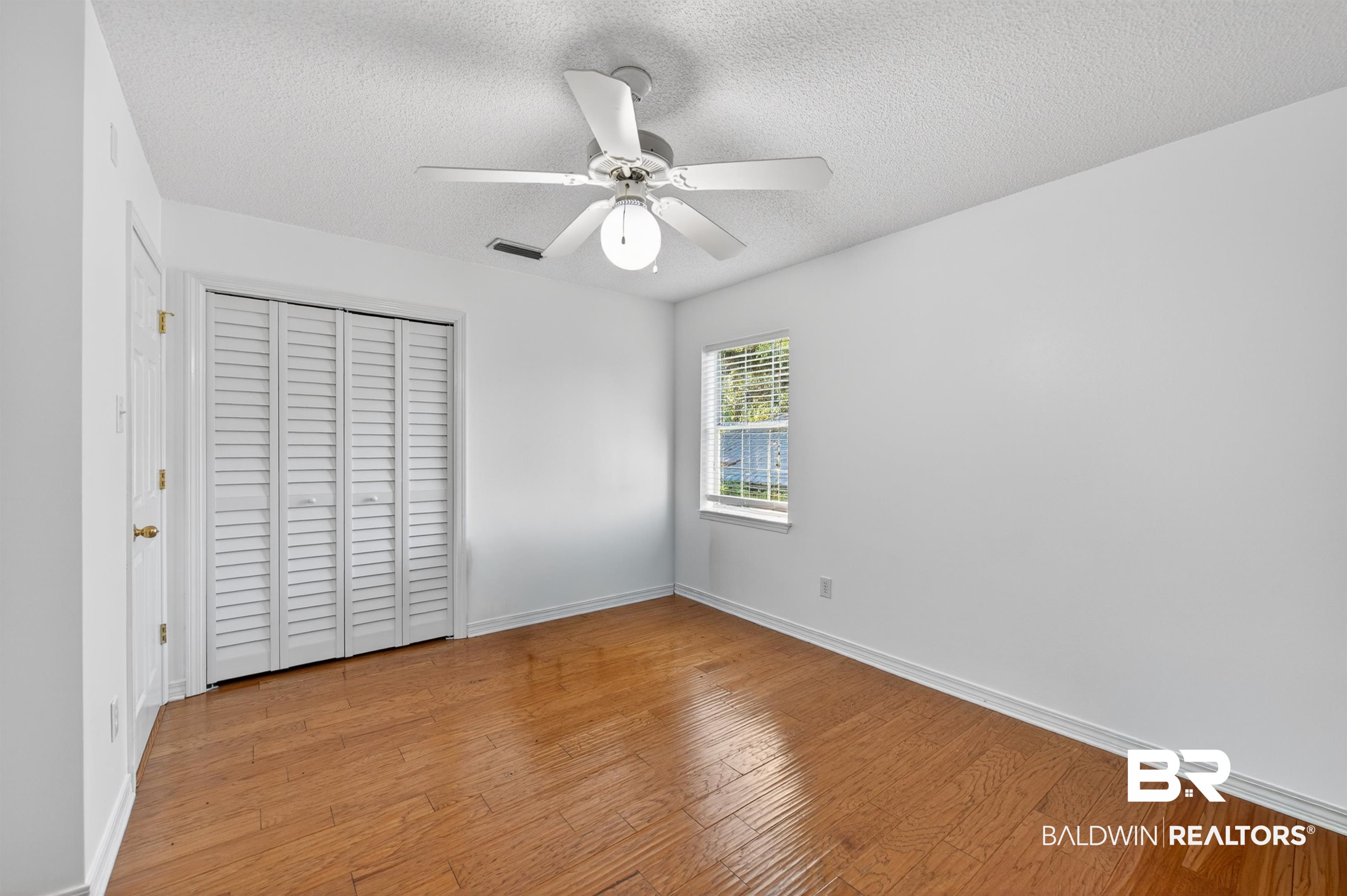 9624 North Bay Street Foley, AL 36535 - Photo 33 of 59 Room featuring wood-finish flooring, a window with blinds, a white ceiling fan with integrated lighting, and a bi-fold louvered closet door