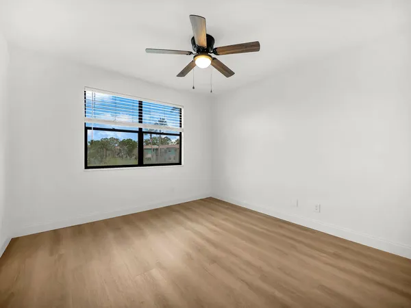 an empty room with wooden floor ceiling fan and windows