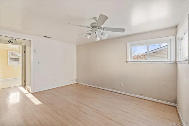 an empty room with wooden floor ceiling fan and windows