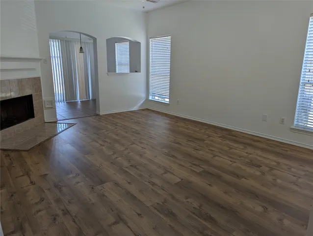 a view of an empty room with wooden floor fireplace and a window
