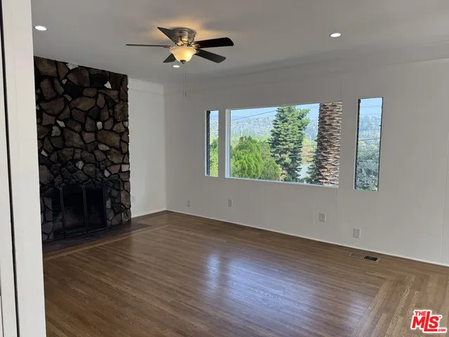 an empty room with wooden floor chandelier fan and windows