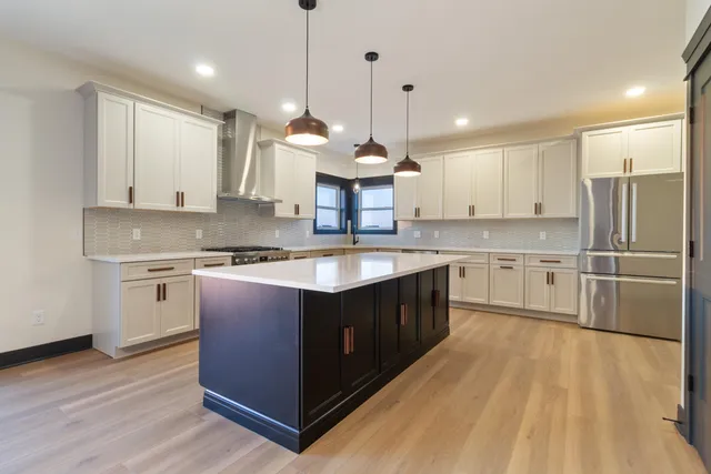 a kitchen with stainless steel appliances granite countertop a sink a stove a refrigerator and island with wooden floor