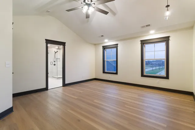 an empty room with wooden floor chandelier fan and windows