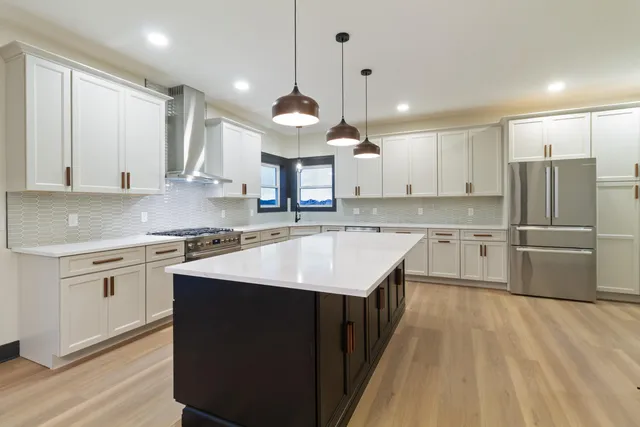 a kitchen with stainless steel appliances granite countertop a sink a stove a refrigerator and island with wooden floor