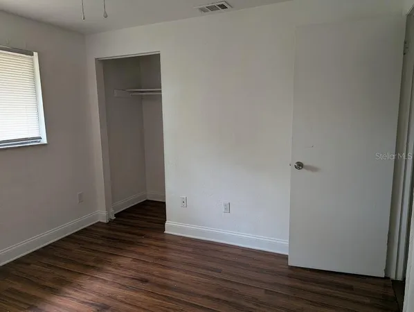 a view of an empty room with wooden floor and closet