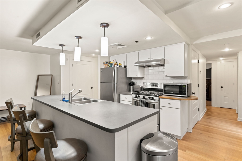 10 Linwood Street Boston, MA 02119 - Photo 21 of 33 a kitchen with a sink a stove a refrigerator and white cabinets with wooden floor