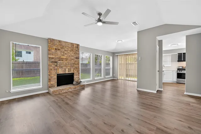 an empty room with wooden floor fireplace and windows