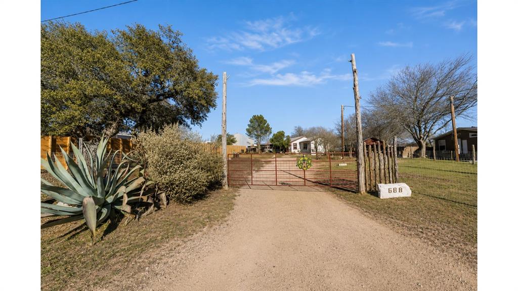 117 Reading Avenue North Center Point, TX 78010 - Photo 20 of 20 Gravel driveway leading to a metal gate entrance, framed by mature trees and native desert landscaping