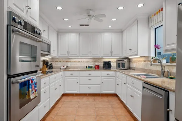 a large kitchen with stainless steel appliances granite countertop a sink and dishwasher a stove top oven with white cabinets