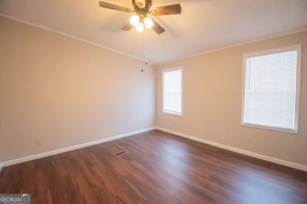 an empty room with wooden floor fan and windows