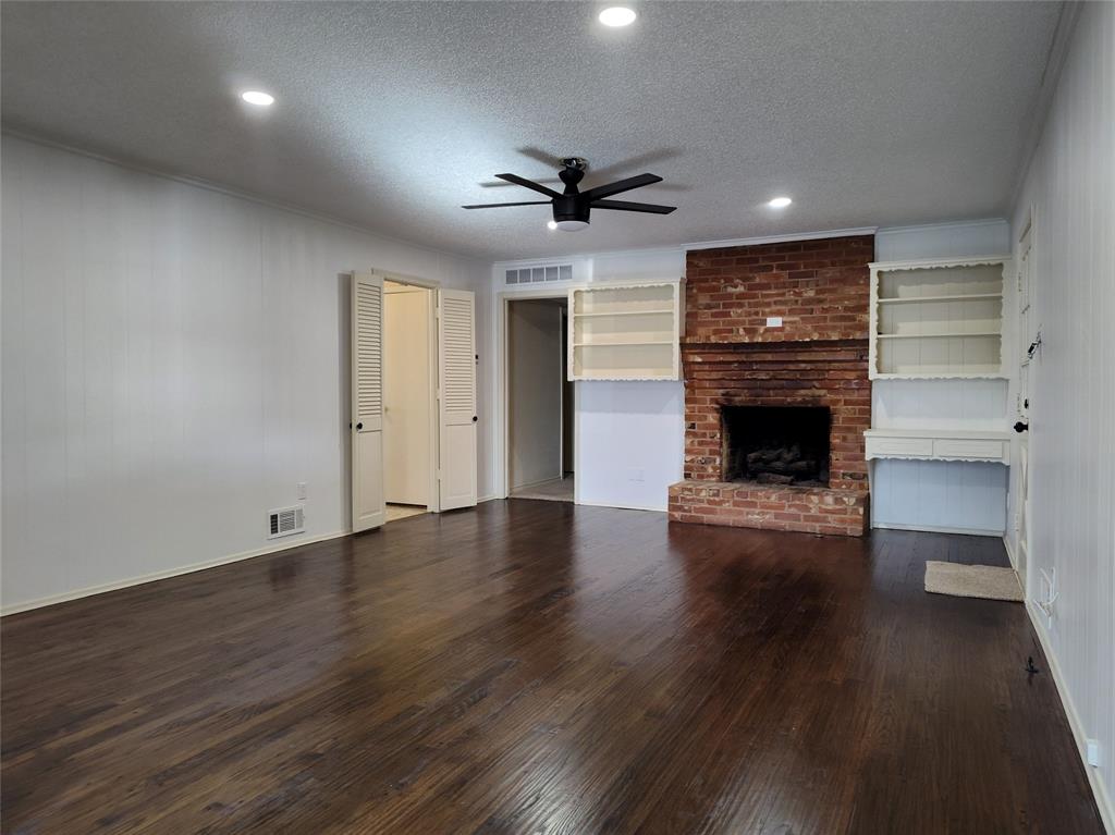 910 Worcester Lane Garland, TX 75040 - Photo 10 of 15 an empty room with wooden floor a ceiling fan a fireplace and windows