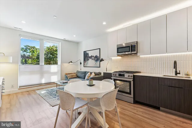 a kitchen with stainless steel appliances granite countertop a stove top oven a sink a refrigerator white cabinets and wooden floor