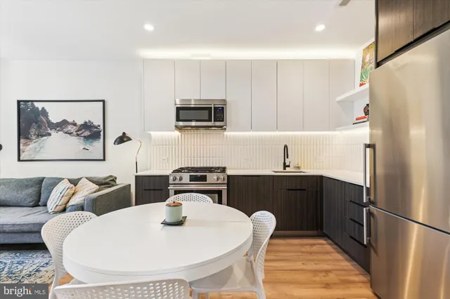 a kitchen with stainless steel appliances a refrigerator a sink a stove a dining table and chairs with wooden floor