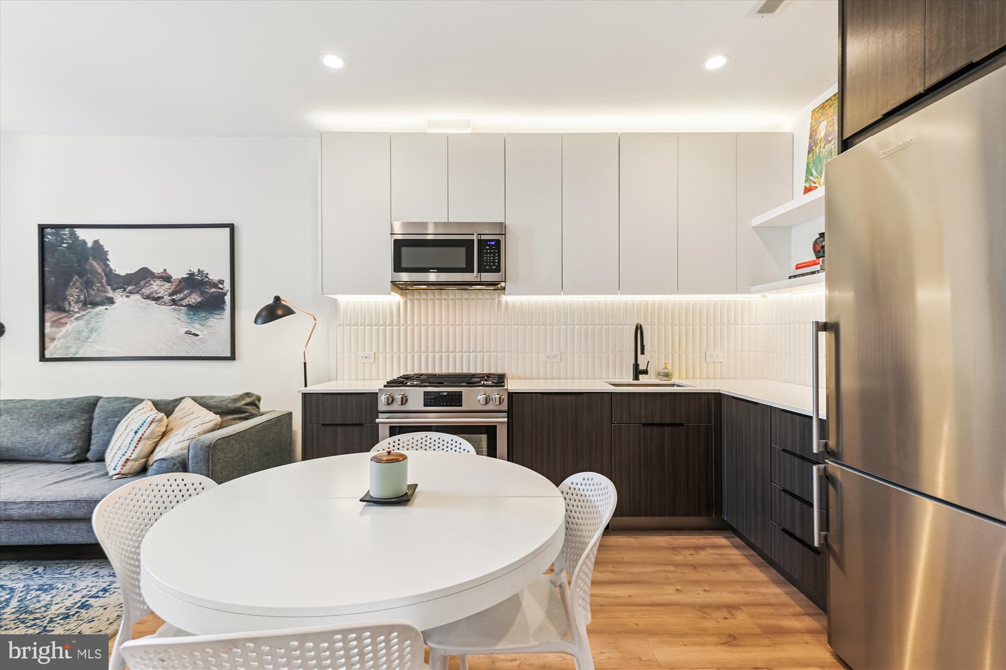 3117 Georgia Avenue Northwest, Unit 102 Washington, DC 20010 - Photo 4 of 30 a kitchen with stainless steel appliances a refrigerator a sink a stove a dining table and chairs with wooden floor