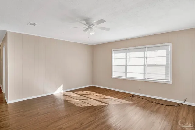 an empty room with wooden floor fan and windows