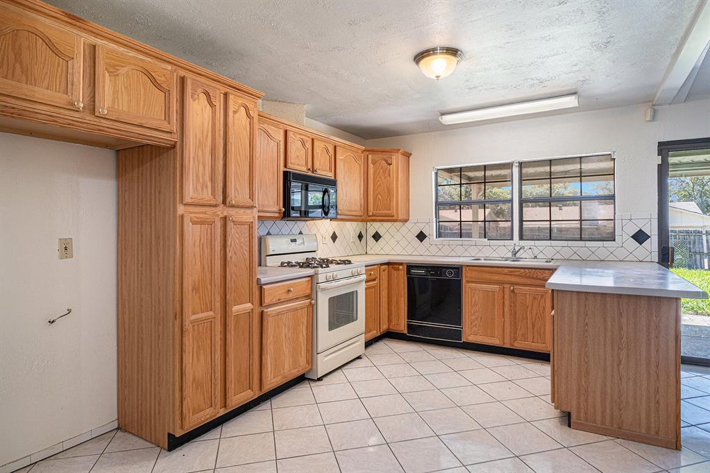 1814 Addington Drive Carrollton, TX 75007 - Photo 11 of 24 Kitchen with light tile flooring, a textured ceiling, black appliances, backsplash, and sink