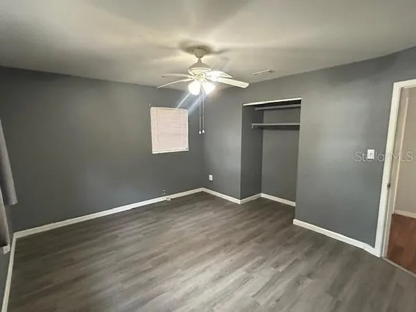 an empty room with wooden floor chandelier fan and windows
