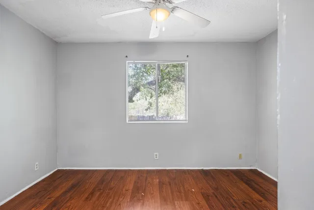 an empty room with wooden floor chandelier fan and windows