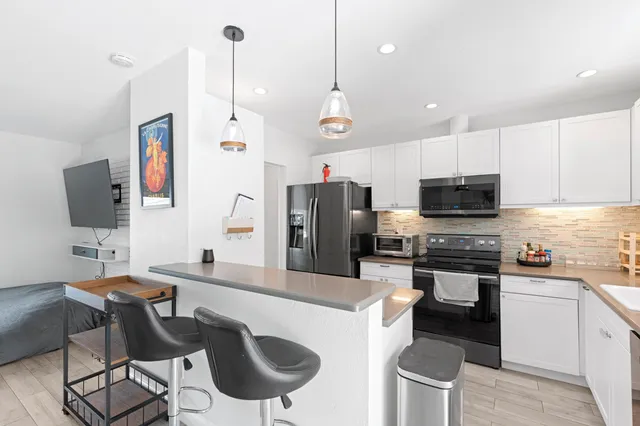 a kitchen with stainless steel appliances granite countertop a stove top oven a refrigerator a sink a dining table and chairs with wooden floor