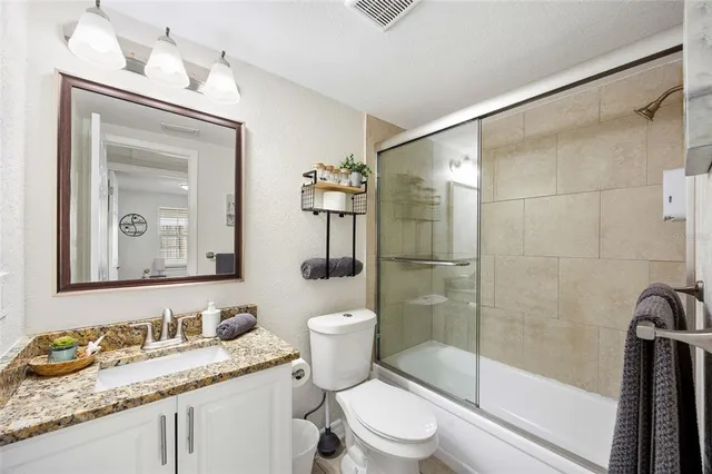 a bathroom with a granite countertop sink a mirror a toilet and shower