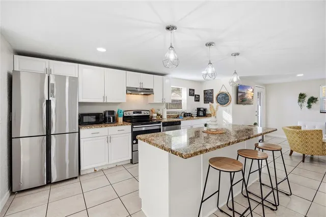 a kitchen with stainless steel appliances granite countertop a refrigerator a sink dishwasher a dining table and chairs with white cabinets