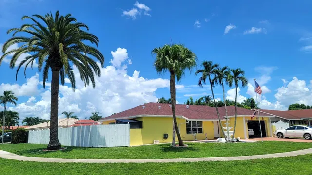 front view of house with a yard and palm trees