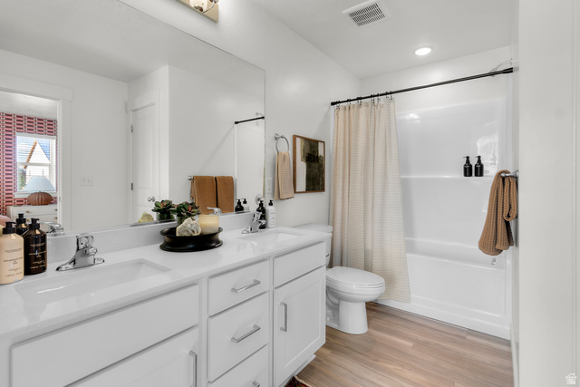 3074 South 270 West Logan, UT 84321 - Photo 26 of 30 Dual vanity with undermount sinks and white cabinetry, expansive mirror, wood-finish flooring, and a shower/tub combination with a black rod