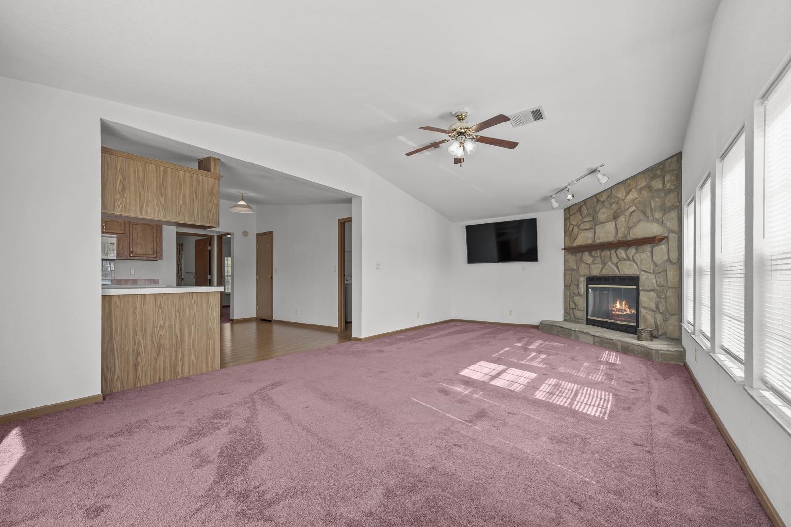 305 Palmetto Bluff Road Palatka, FL 32177 - Photo 9 of 34 Unfurnished living room featuring rail lighting, a stone fireplace, vaulted ceiling, carpet flooring, and ceiling fan