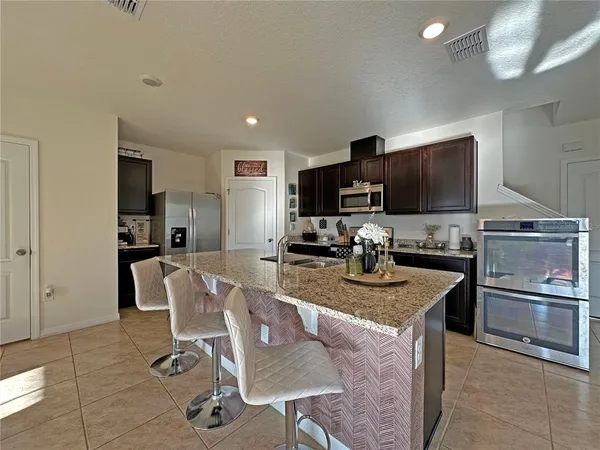 a kitchen with stainless steel appliances granite countertop a sink a stove a refrigerator cabinets and chairs