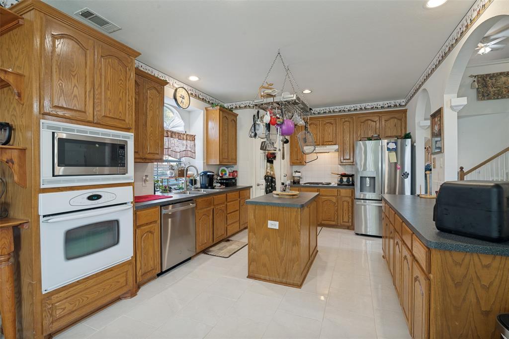 2213 Ranch Road Sachse, TX 75048 - Photo 8 of 28 Kitchen with wood-finish cabinetry, white tile flooring, built-in stainless steel microwave and oven, and a central island
